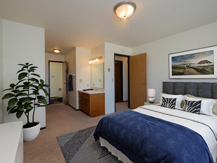 a bedroom with a large bed and a potted plant. Fargo, ND Countryside Apartments